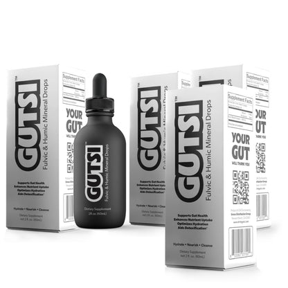 A bottle of GUTSI liquid-boosting mineral drops stands in front of several white and gray product boxes on a clean white background. The bottle has a black dropper cap, and the packaging features large black GUTSI branding and supplement facts panels.